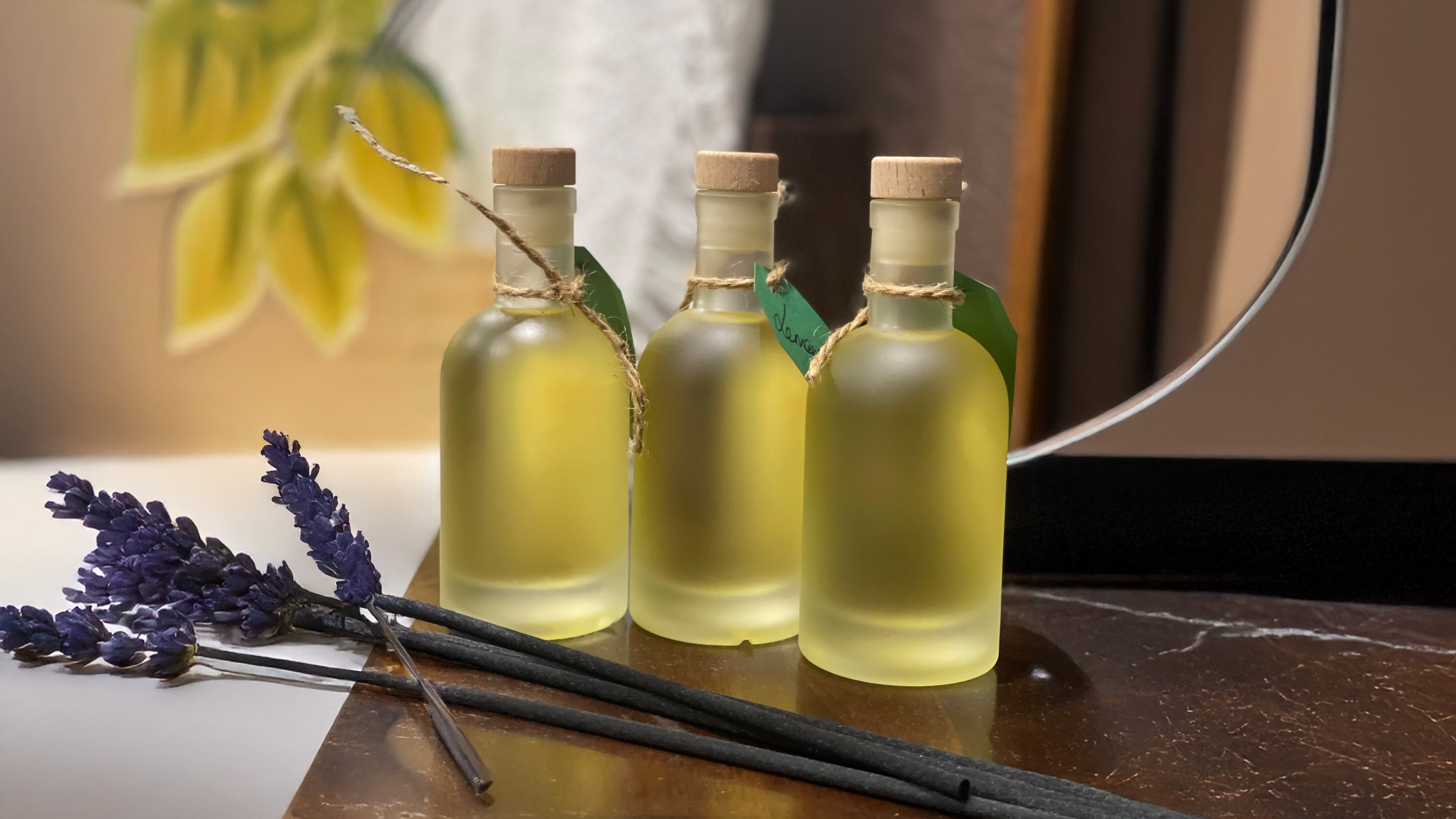 Three small bottles of diffuser on a wooden surface with lavender and a mirror in the background.