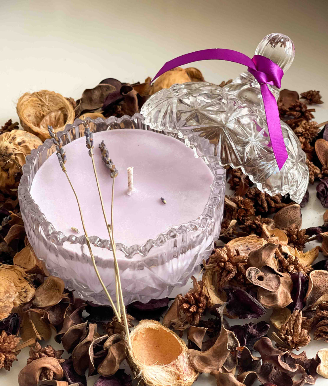 Candle in a decorative glass holder with a purple ribbon surrounded by dried flowers and leaves.